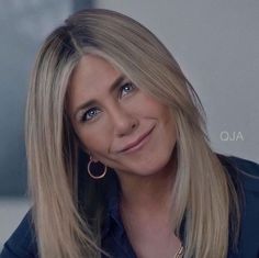 a woman with blonde hair and blue eyes smiles at the camera while wearing gold hoop earrings