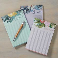 three notepads with flowers on them sitting next to a pen and paper pad