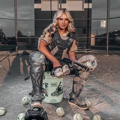 a woman sitting on top of a bucket filled with baseball balls and catchers mitts