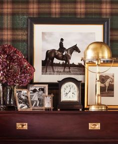 there is a clock, vase with flowers and pictures on the shelf next to it