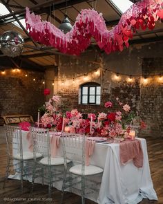 the table is set with pink and red flowers, candles, and hearts hanging from the ceiling