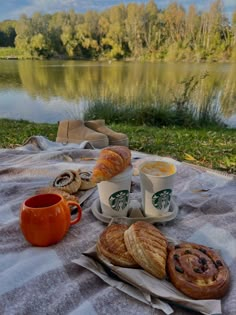 coffee, croissants and other pastries are sitting on a blanket near the water