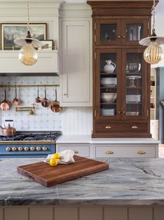 a kitchen with marble counter tops and wooden cabinetry, hanging lights over the stove