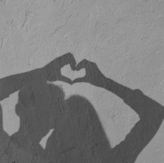 a shadow of a person making a heart shape with their hands on the wall behind them