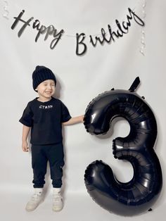 a young boy standing in front of a happy birthday sign with an inflatable number