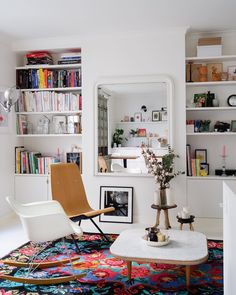 a living room filled with furniture and bookshelves next to a white table topped with flowers