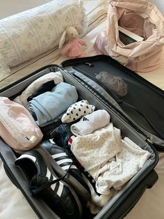 an open suitcase filled with clothing and shoes on top of a white sheet covered bed