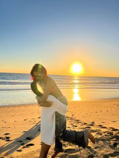 a man and woman hug on the beach at sunset