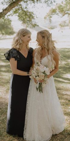 two women standing next to each other in front of a tree and grass covered field