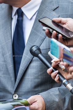 a man in a suit and tie is holding a microphone while looking at his cell phone