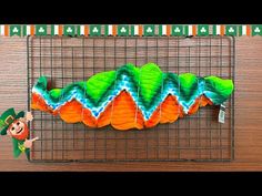 an orange and green cake sitting on top of a wire rack next to a paper lepreti