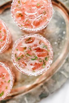 three glasses filled with watermelon and garnish on top of a metal tray