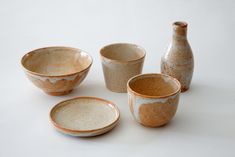 four ceramic bowls and two vases on a white surface