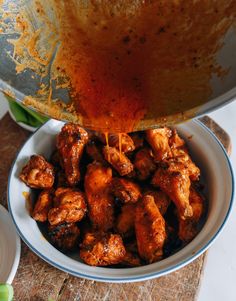 someone is pouring sauce on chicken wings in a bowl