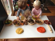 two young children sitting at a table with bowls and plants in front of them,