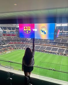 a woman standing in front of a large screen at a soccer stadium holding her hand up