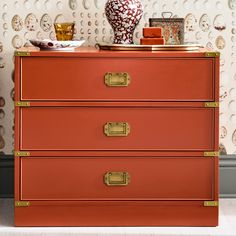 an orange dresser with gold handles in front of a wallpapered background and vase