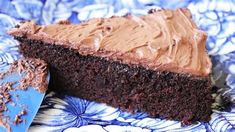 a piece of chocolate cake with frosting on a blue and white plate next to a knife