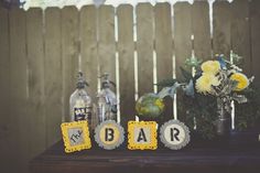 a table topped with vases filled with flowers next to bottles and signs that spell out the word bar