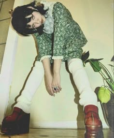 a woman in green dress sitting on top of a wooden floor next to a potted plant