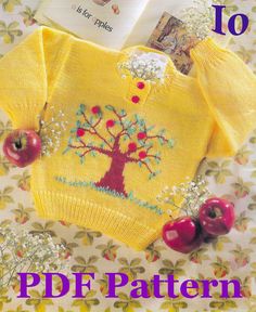 a yellow sweater with an apple tree on it and two cherries in the background