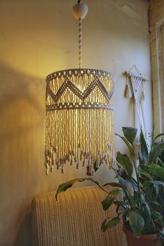 a lamp hanging from the ceiling next to a potted plant on a couch in front of a window