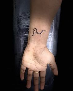 a person's hand with the word dad tattooed on their left wrist, in black ink