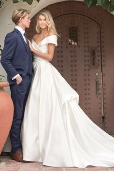 a man and woman standing next to each other in front of a door wearing wedding gowns