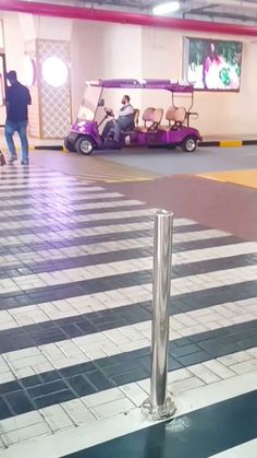 a man standing next to a purple golf cart in a parking garage with people walking by