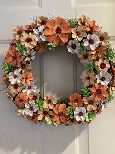 an orange and white wreath hanging on a door with flowers in the center that is made out of paper