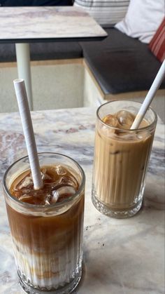 two glasses of iced coffee sitting on a marble table with a white straw sticking out of the top