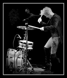 a woman playing the drums on stage in front of a microphone and drum set with her legs spread out