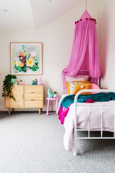 a pink canopy bed sitting in a bedroom next to a dresser and table with flowers on it