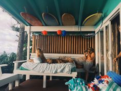 two women sitting on a porch with surfboards hanging from the roof and one woman laying down