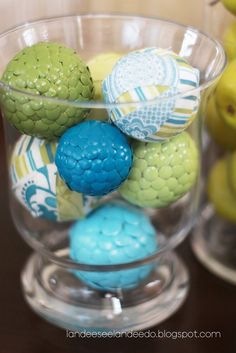 some colorful balls in a glass bowl on a table with other items around it and one is yellow, blue, and green