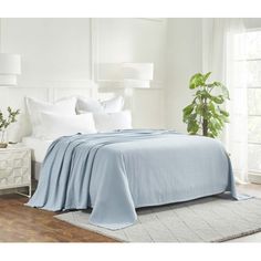 a bed with white sheets and pillows in a bedroom next to a plant on the floor