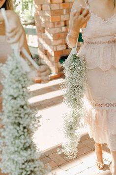 a woman in a white dress holding a bouquet of baby's breath flowers while standing next to another woman