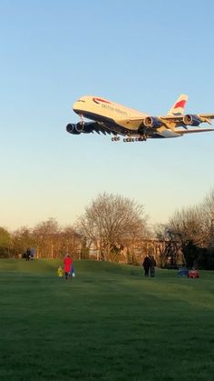 an airplane is flying low over the grass as people walk by onlookers