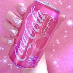 a woman's hand holding up a pink soda can with glitters on it