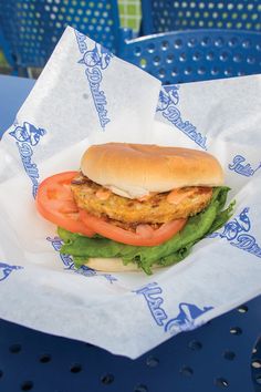 a chicken sandwich with tomatoes and lettuce in a paper wrapper on a blue table