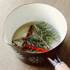 a pot filled with carrots and herbs on top of a wooden table next to a knife