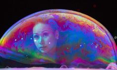 a woman's face is reflected in a bubble like object that appears to be floating on water