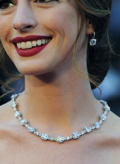 a woman wearing a necklace and earrings smiles at the camera as she stands in front of an audience