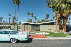 an old car is parked in front of a house with palm trees on the street