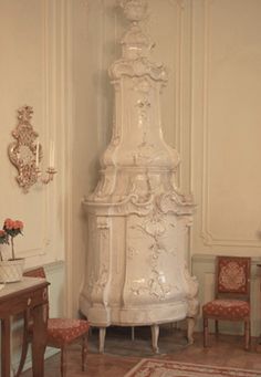 a tall white clock sitting in the corner of a room next to a table and chairs