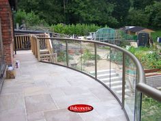 an outdoor patio with glass railings and plants on the side of the building, surrounded by greenery