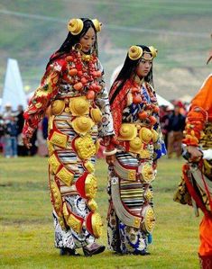 two women dressed in traditional japanese clothing walking on the grass with other people behind them