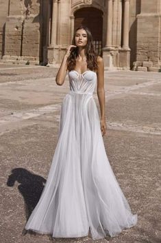 a woman in a white wedding dress standing on an empty lot with her hand up to her face