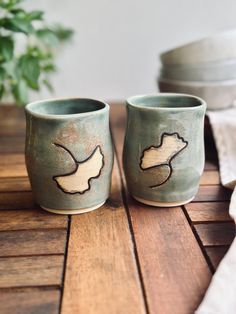 two cups sitting on top of a wooden table next to a potted green plant