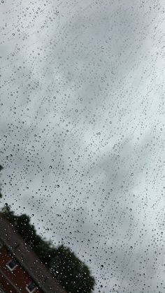 raindrops on the window with buildings in the back ground and cloudy sky above